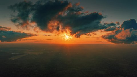 Aerial view of epic dark clouds flying into camera, revealing scenic sunset sun setting into horizon. Timelapse, 4K UHD.	
