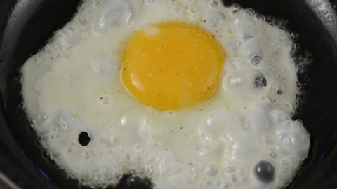 Fried eggs in a pan. The broken egg falls into the frying pan and is sprinkled with spices.