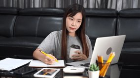 4k video of Attractive beautiful asian woman working with laptop and document at the indoors living room office as a freelancer, e-coaching working, remotely or work from home concept