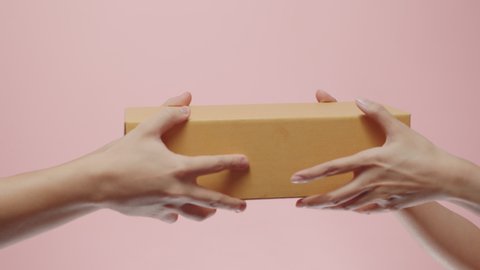 Close up of Woman's Hand Receive a parcel cardboard box from a delivery man who gives her Postal Package Box isolated on a pink studio background. Shipping and Delivery Concept.