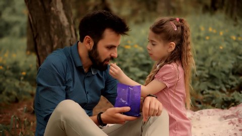 Adorable Daughter Kid With Father Eating Sweets. Daughter With Cheerful Father Eat Candy. Happy Beautiful Family Relaxing Together In Park. Little Cute Preschool Girl Having Fun And Eats Jelly Candies स्टॉक वीडियो
