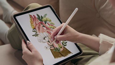 Art of young woman drawing environmental image at tablet close-up indoors. Caucasian artist sketching color flowers in hands at screen of digital pad. Draw ecological painting by stylus at pretty home