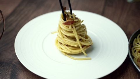 Preparing and decorating spaghetti/pasta with a ladle from a pan full with spaghetti carbonara into a serving white plate