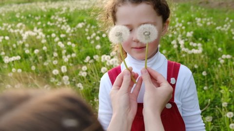 Side view of unrecognizable young mother having fun with playful preschool daughter outdoors during sunset, cute little girl blowing dandelion on her mom in summer park. Slow motion Arkivvideo