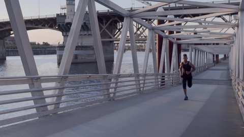 Athlete Sprints Up Pedestrian Bridge Toward Camera, At Sunset On The Willamette River (Slow Motion)