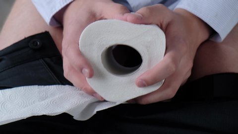 A man squeezes toilet paper in his hands, experiencing pain from hemorrhoids during bowel movements