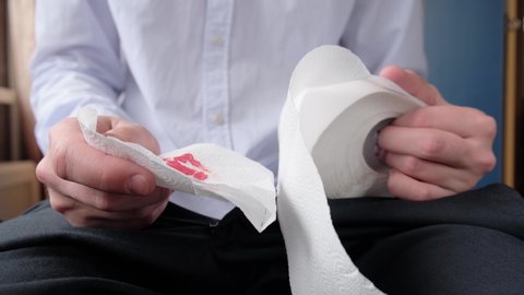 A man squeezes toilet paper with blood in his hands, experiencing pain from hemorrhoids, closeup