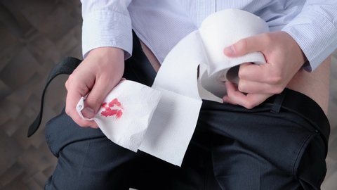 A man with hemorrhoids squeezes toilet paper with blood. Concept: hemorrhoids, colon tumor, irritable bowel syndrome, diarrhea, poisoning