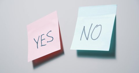 Close-up of a female hand tearing off a blue sticker with the word No, leaving a pink sticker with the word Yes on a gray board. The concept of choice.