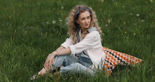 girl with curly hair sits on the grass and smiles