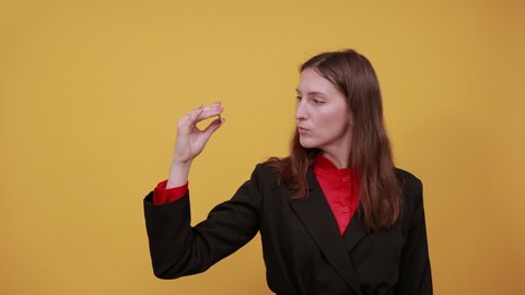 Young Attractive Woman Brunette In Black Stylish Suit, Red Shirt On Yellow Background, Successful Woman Holds A Bitcoin Coin In Her Hand, Smiles. The Concept Of Wealth, Business And E-Commerce