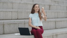 Joyful businesswoman having video chat with friend on smartphone at street. Positive girl using cellphone for video call outside. Happy woman showing wedding ring at phone camera