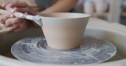 Female potter paints rotating pot on the pottery wheel. Arkistovideo