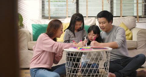 Happy young asian family parents and cute little children drawing coloring picture with pencils helping cute child daughter enjoying talk play at home, mom dad and kid girl having fun in living room.