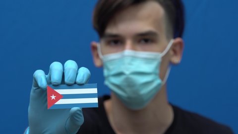 COVID-19 pandemic in Puerto Rico. A young, attractive Puerto Rican man, Latin American, wearing a protective medical mask and gloves. The guy is holding the flag of Puerto Rico. Coronavirus disease