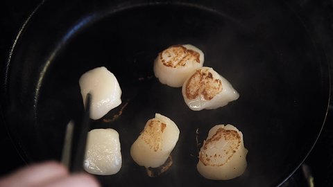 the chef is cooking scallops. Scallop is cooking in a pan. Someone's cooking seafood. Close-up of the scallop.