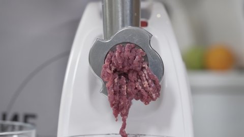 Filling comes out through raw meat grinder sieve. Grinder closeup. Electric mincer machine with fresh chopped meat. Process of meat grinding in kitchen with mincing machine. Preparation of minced beef