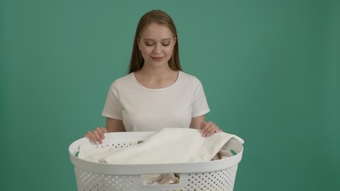 Happy woman with clean laundry in basket on color background