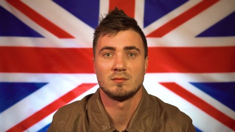 An attractive man against the background of the flag of Great Britain looks at the camera and blows a kiss. Friendly british