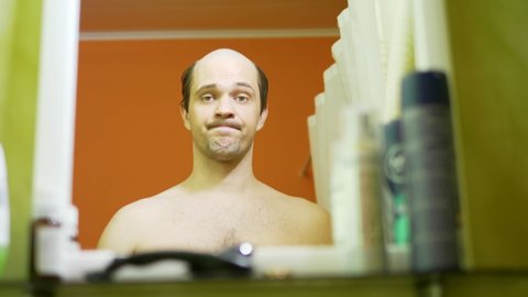 balding narcissistic man looks in the mirror in the bathroom. closeup.