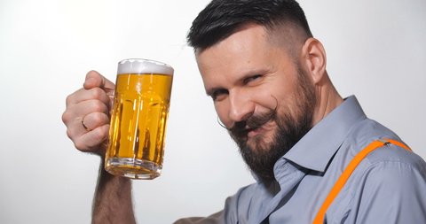 Close up side view portrait of handsome bearded man with long twisted mustache, toast, drinking beer from large glass mug on white background isolated. With free space for writing 4k slow motion.