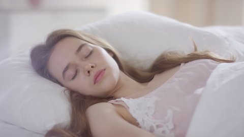  Slowmo shot of beautiful young woman in nightdress waking up in bed on tranquil morning