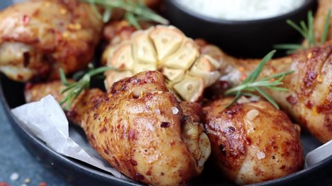 Baked spicy chicken legs with rosemary and garlic on black slate, dark background.