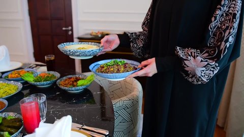 The Islamic holiday of Eid ul-Fitr marks the end of the Islamic fasting of the month of Ramadan.Traditional Eastern food and meal are on the table. Woman puts a plate of food on the table