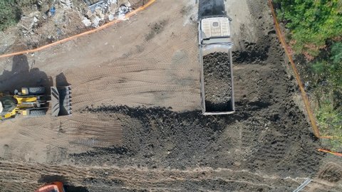 Loading dirt, debris and junk on truck container. Aerial shot above excavator tractor load construction site waste on truck for dumping. heavy machinery industry equipment transportation