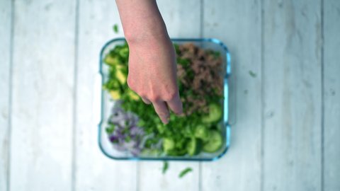 A close-up look of a woman's hand dressing a salad with chopped fresh cilantro/coriander. Concept of preparing a healthy salad in a glass bowl.