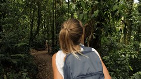 Rear view of young woman walking in tropical rainforest exploring nature and enjoying national park. People travel exotic destination