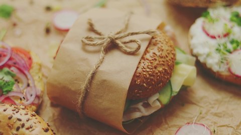 Close up shot. Bagels with Italian ham prosciutto, cream cheese, hummus, radish and salad wrapped in brown baking paper ready for take away. Healthy breakfast concept. Side view.