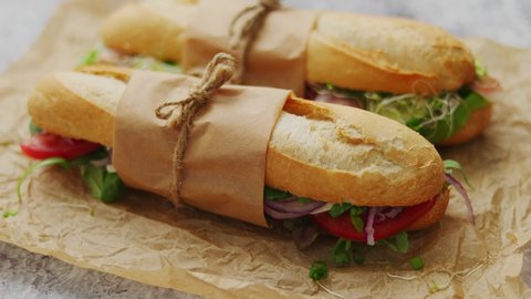 Tasty homemade sandwiches Baguettes bread with various healthy ingredients. Olives, tomatoes, ham, lettuce, garlic and spices over brown baking paper. Take away option. Breakfast take away concept