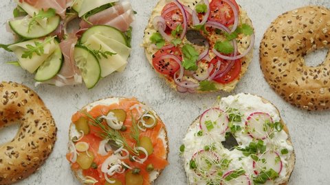 Homemade Bagel sandwiches with different toppings, salmon, cottage cheese, hummus, ham, radish and fresh herbs on a white rusty table, top view. Delicious and healthy breakfast concept.