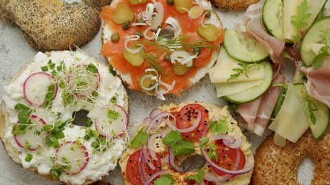 Bagel sandwiches with various toppings, salmon, cottage cheese, hummus, ham, radish and fresh herbs on a white rusty table, top view. Delicious and healthy breakfast concept.