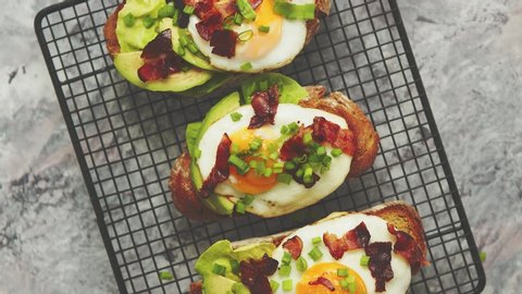 Breakfast concept. Tasty delicious homemade toasts with fried egg, bacon, avocado, lettuce and chive. Served on black grill