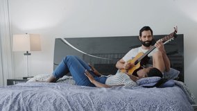 Mixed couple enjoy music in bedroom. Happy black woman singing song and white man playing guitar in bed. Married life and recreation for smiling partners - Powered by Shutterstock - Get 15% off with code: PIKWIZARD15