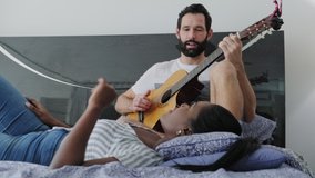 Interracial couple enjoy music in bedroom. Happy black woman singing song and white man playing guitar in bed. Lifestyle and relaxation for married partners - Powered by Shutterstock - Get 15% off with code: PIKWIZARD15