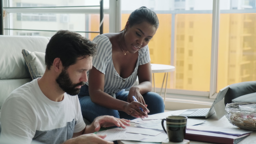 Multiethnic couple filing tax return, preparing home budget. African American woman and Caucasian man checking utility bill and banking account. Married people preparing taxes and form | Shutterstock HD Video #1053104507
