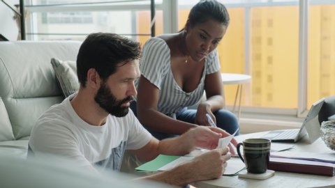 Multiethnic couple filing tax return, preparing home budget. African American woman and Caucasian man checking utility bill and banking account. Married people preparing taxes and form