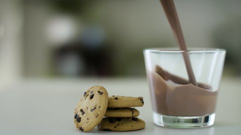 Chocolate milk pouring into a glass beside tasty cookies. Shot in slow-motion on RED camera in 4k.