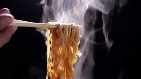 Chopsticks to tasty noodles with steam and smoke in 4K Resolution on dark background, Asian meal close-up, Hot food and fast food concept