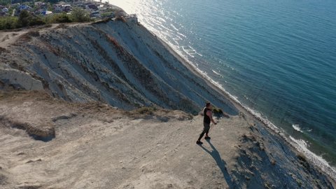 Aerial view of man training with rubber bands on top of cliff, beautiful view of sea and landscape. Athlete trains his muscles and body outdoors