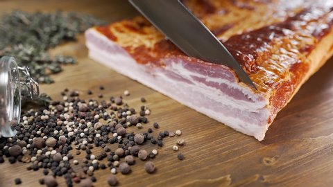 chef cuts pieces of smoked bacon by sharp knife on the wooden board