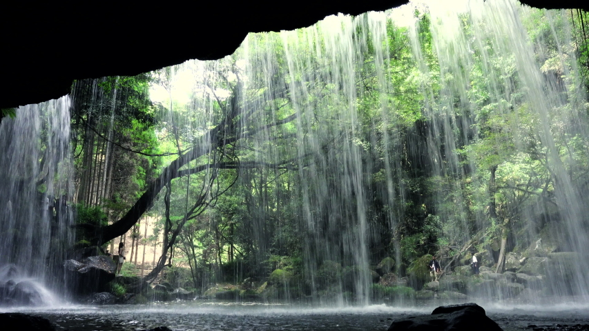 Silhouette of a man standing behind a curtain of water at Nabegataki Falls Kumamoto waterfall in a forest in Japan Royalty-Free Stock Footage #1053131669