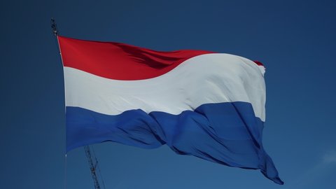 Horizontal view of the largest flag of the Netherlands. Large Dutch flag with red, white and blue colours hoisted in a crane, slowly waving in the wind, blue sky. Celebration, Kingsday, Liberation day