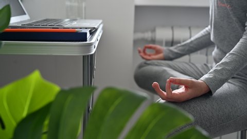 Young woman is meditating at home in her home office. Close up of woman's hands. Concept of relaxation and meditation.