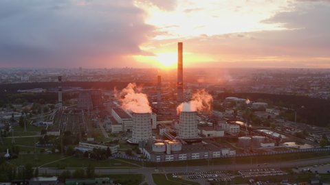 Aerial view industrial area, drone flies over power plant just before sunrise. Thermal power station and factories in orange sun light. Industrial district from above, smoke pipes, big city on horizon