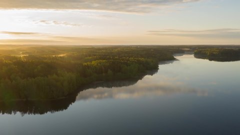 Hyperlapse drone flying over lake at sunrise. Timelapse clouds of fog above water surface. Early morning haze. Haze over river countryside. Pine trees forest on horizon reflected in water