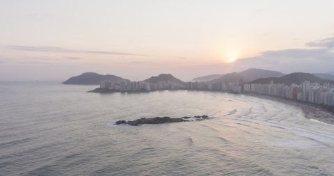 Aerial hyperlapse of sunset at beach surrounded by buildings. Waves and people moving. Pitangueiras, Guaruja, Sao Paulo, Brazil